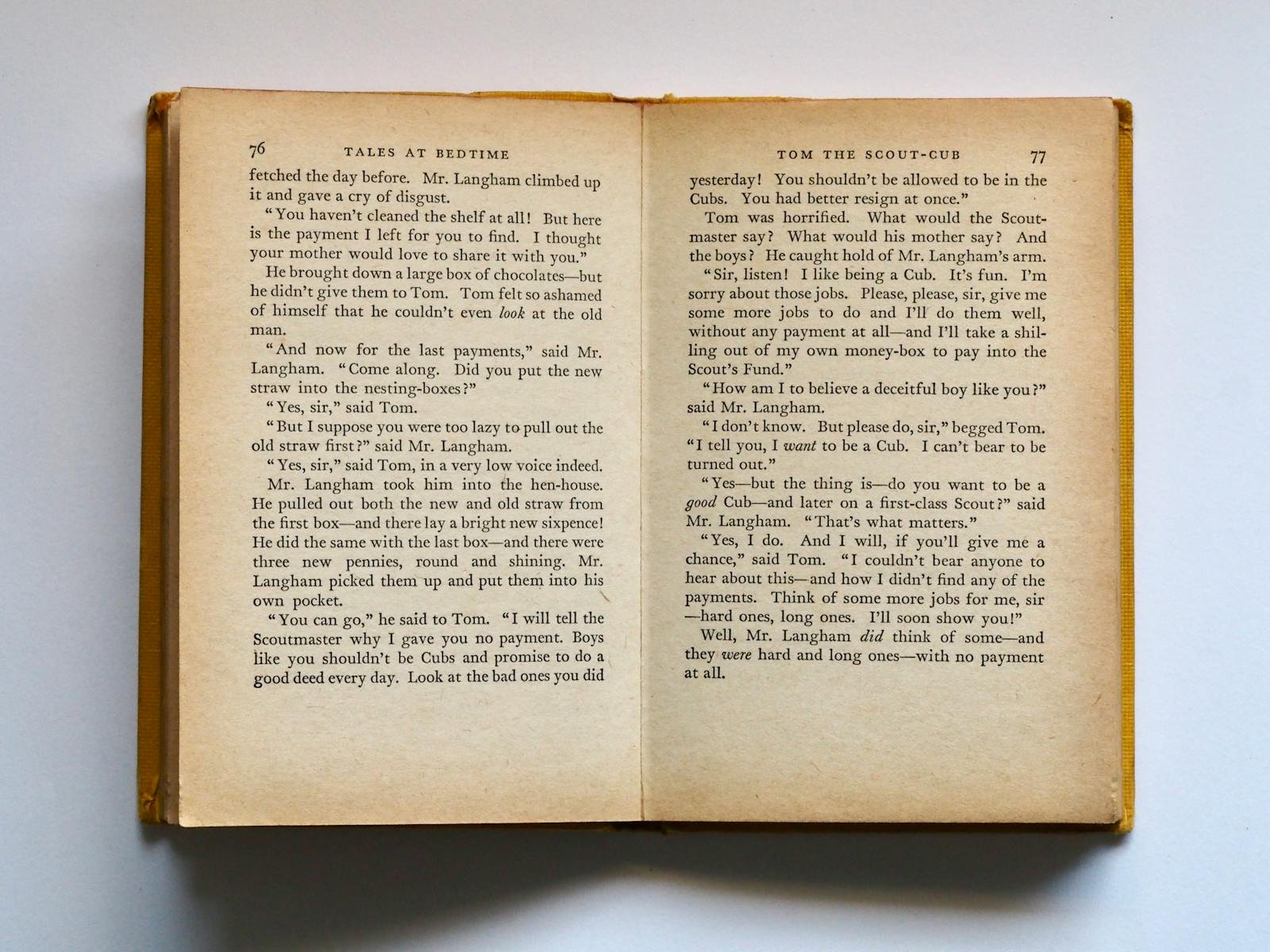 Vintage book opened to pages 76-77, displaying classic literature text in soft lighting.